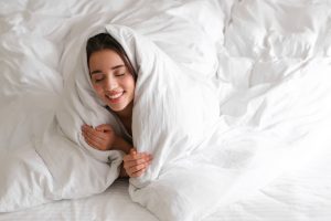 Cheerful,Young,Woman,Covered,With,Warm,White,Blanket,Lying,In
